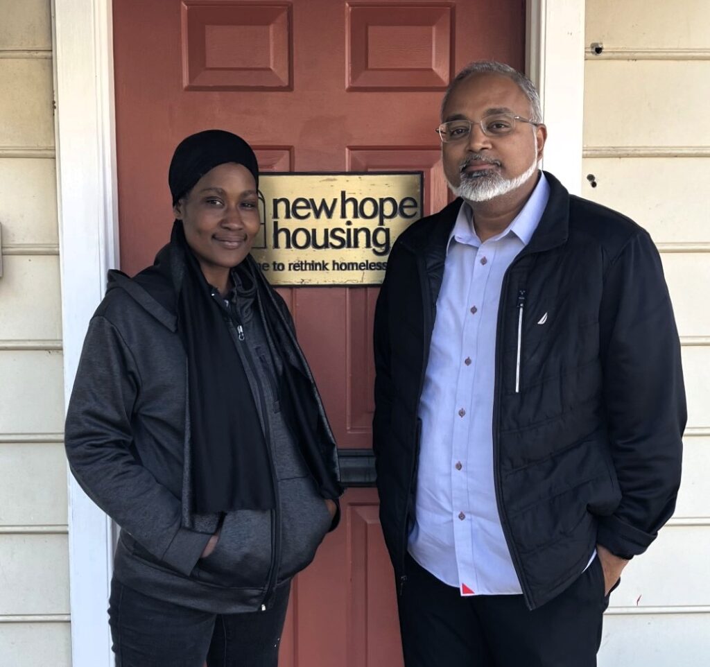 Two individuals standing in front of a red door with a sign that says New Hope Housing