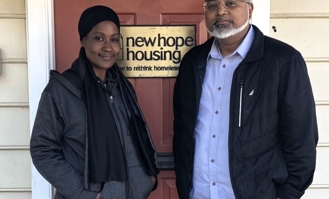 Two individuals standing in front of a red door with a sign that says New Hope Housing