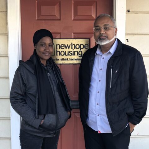 Two individuals standing in front of a red door with a sign that says New Hope Housing
